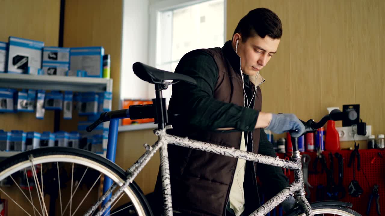 el personal de servicio profesional está arreglando el manillar de la bicicleta, girando la llave de allen para apretar la articulación y escuchando música con auriculares. son visibles herramientas especiales, repuestos y equipos.
