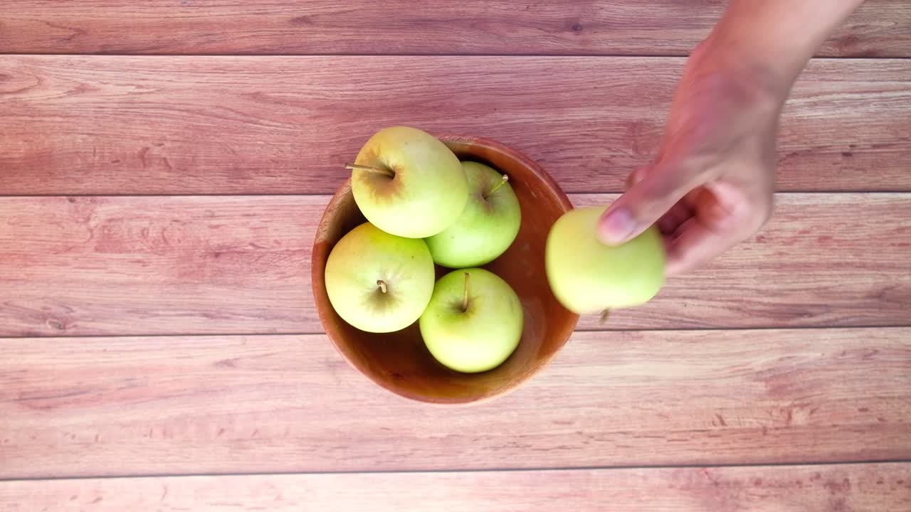 Mano che prende una mela verde da una ciotola di legno