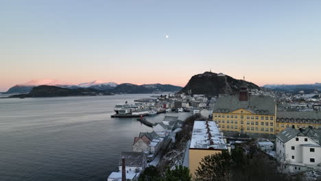 Norway-4K-Aerial-of-Ålesund-in-winter-slowly-ascending-from-behind-a-tree-to-reveal-the-harbour-and-a-beautiful-sunset