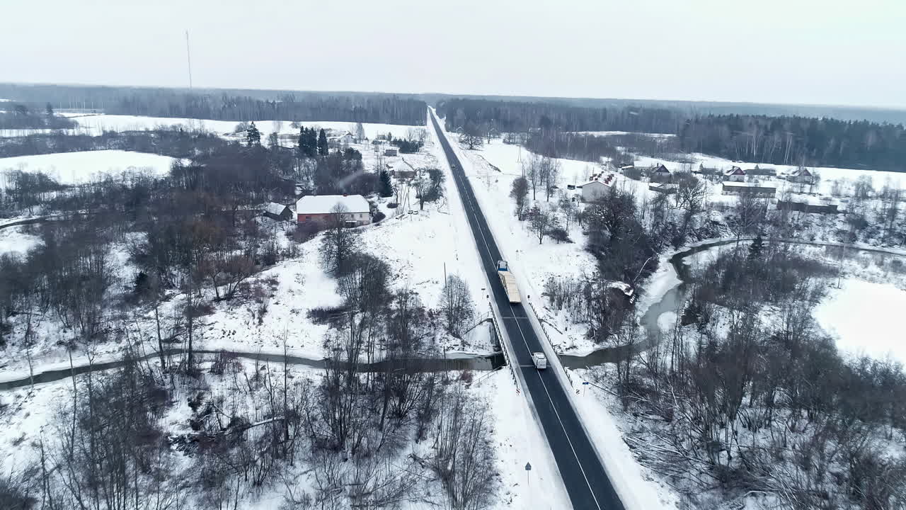 눈 덮인 풍경 속에서 시골길을 따라 운전하는 목재를 실은 긴 트럭