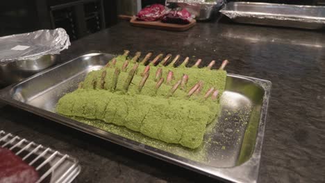 venison meat ribs in green color spice, on a metal tray on kitchen table, before baking in oven