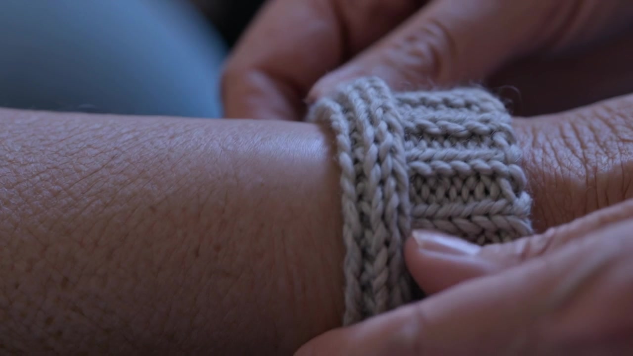 Mani che aiutano a sistemare, facendo scivolare un polsino di maglia sul polso del destinatario nel seggiolino auto, fissandolo saldamente.
