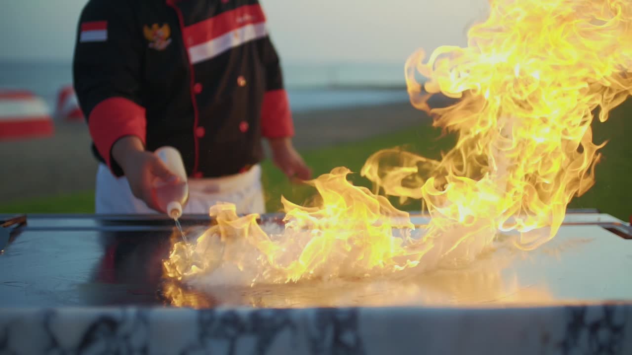 The cook pours oil on the grill with the art of teppanyaki. and flames come out.