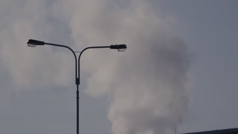 silhouette of a lamppost behind which the menacing smoke of a factory rises