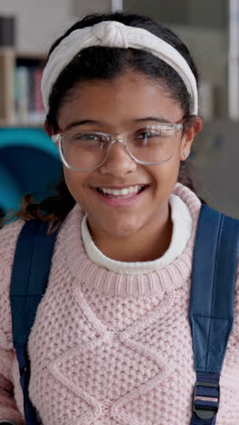 a young girl smiling at the camera while wearing glasses and a backpack