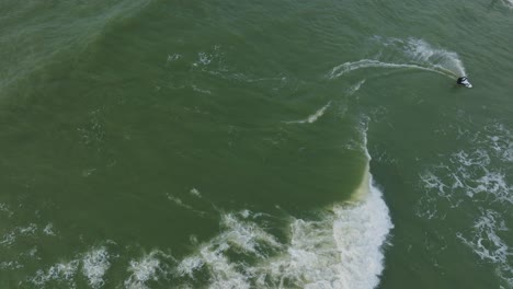 Establishing-aerial-birdseye-view-of-a-man-engaged-in-kitesurfing,-overcast-winter-day,-high-waves,-extreme-sport,-Baltic-Sea-Karosta-beach-,-drone-dolly-shot-moving-right