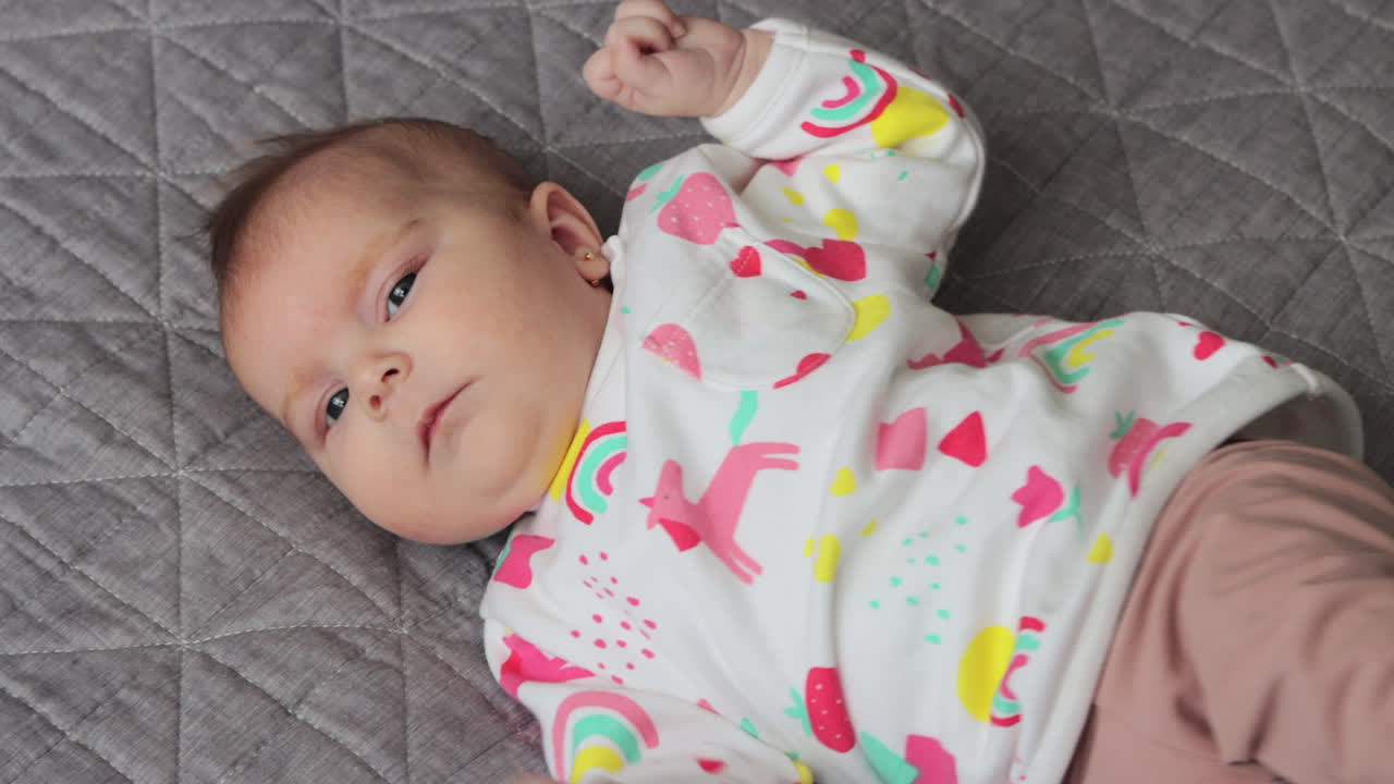 lindo bebé niña acostada sobre la espalda, moviendo los brazos y las piernas, mirando a la cámara