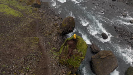 Aerial:-Top-down-shot-of-a-man-standing-on-a-rock-near-a-river