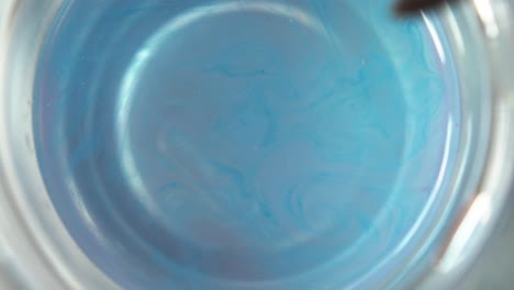 la pintura azul se dispersa de los pelos del pincel de acuarela a medida que se gira en una taza de agua limpia