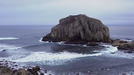 foamy sea waves and flock of birds resting in peña blanca rocky islet on a cloudy day, algarrobo, chile