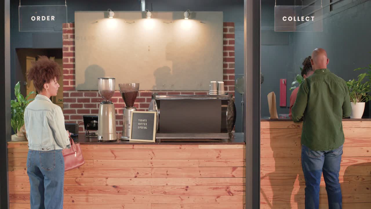 Barista afroamericana prepara una bevanda alla macchina per espresso e consegna la tazza a un uomo che ritira l'ordine