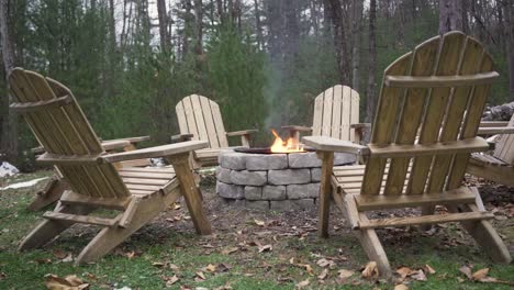 close up of 6 empty lawn chairs around a burning fire pit