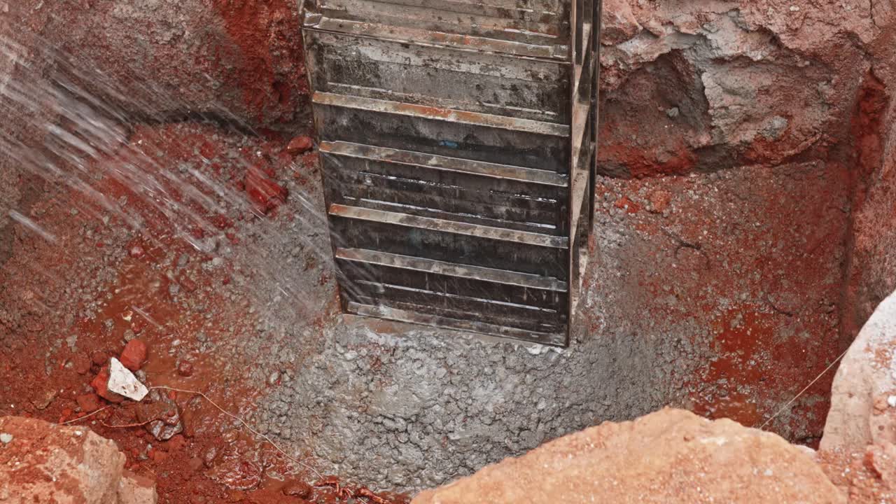 water curing being performed on a freshly poured concrete foundation footing at a construction site. day time, stable shot, top down shot, 4k