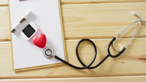 video of stethoscope, clipboard, red heart and glucometer on wooden background with copy space