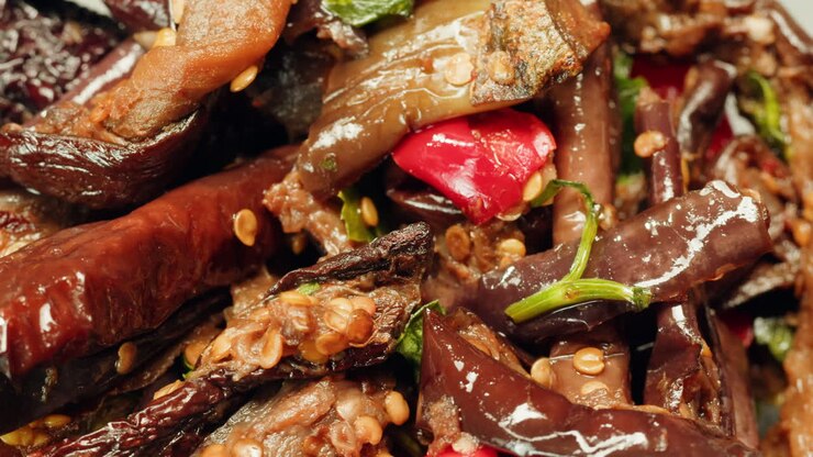 Close-up of fermented eggplants with red sweet pepper and mustard on plate. Preservation of vegetables in glass jars. Fermentation preserved aubergine with hot chilli peppers and greens.
