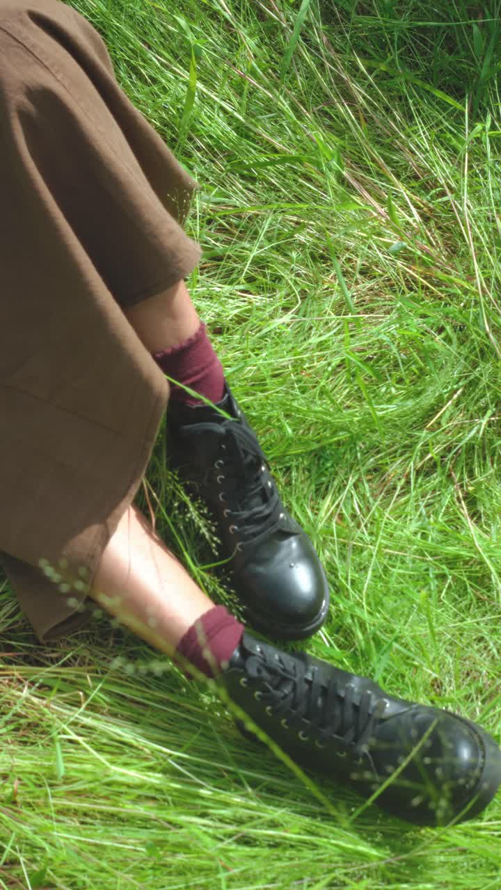 Still vertical close-up of boots, socks and skirt resting in green tall grass