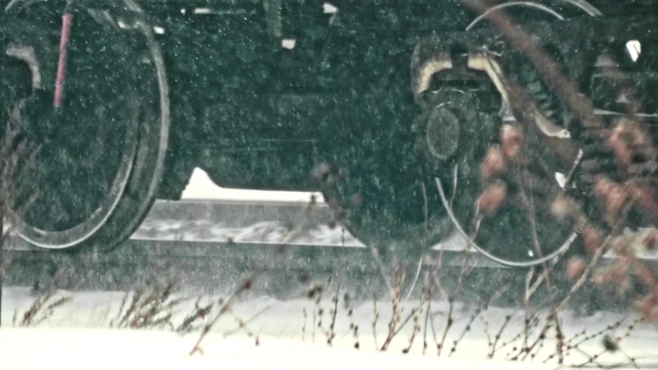 Ruote del treno in movimento su binari ferroviari innevati durante una nevicata invernale.