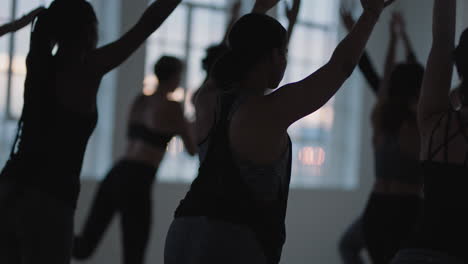 yoga-kursgruppe gemischtrassiger frauen, die kriegerpose praktizieren und einen gesunden lebensstil genießen und bei sonnenaufgang im fitnessstudio trainieren