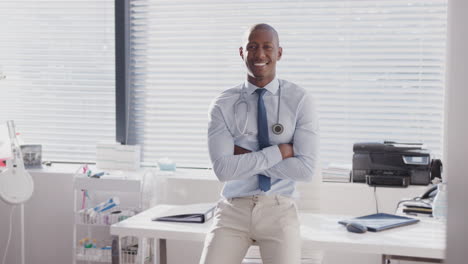 Portrait-Of-Smiling-Male-Doctor-Sitting-On-Desk-In-Office