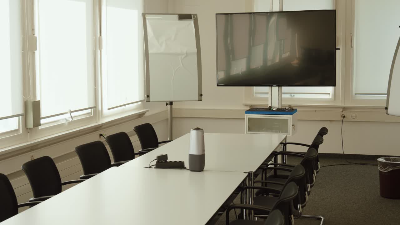 Sala de reuniones luminosa y moderna con mesa larga, sillas, rotafolio y pantalla grande, preparada para una conferencia de negocios, taller o sesión de capacitación corporativa
