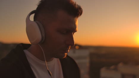 a man freelancer in headphones standing on the roof at sunset writes on the keyboard code pages. little business. listen to music and work at the computer enjoying the beautiful view from the roof.