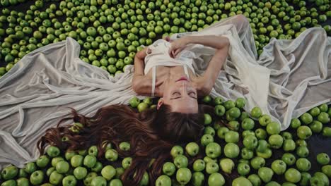 woman in white dress laying on a bed of green apples