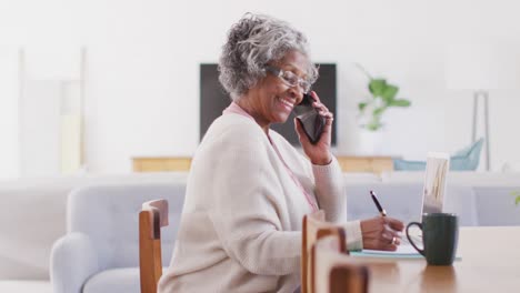 Retrato-De-Una-Feliz-Anciana-Afroamericana-Sentada-En-La-Mesa,-Hablando-Por-Teléfono-Inteligente