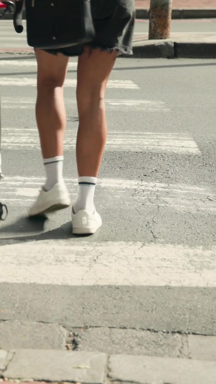 Vertical video: Leaving curb, woman in green top pushing white bike across zebra crosswalk to cross