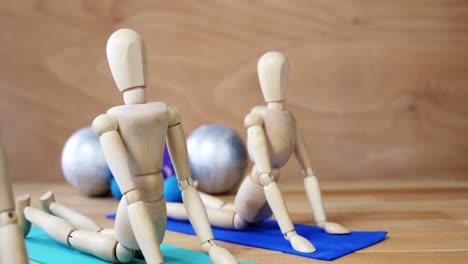 Wooden-figurine-exercising-on-exercise-mat-in-front-of-gym-balls-against-wooden-background