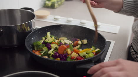 manos de mujer cocinando verduras en una sartén en la cocina