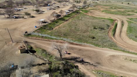 Panning-drone-footage-showing-following-2-Motocross-riders-taking-a-smooth-line-around-a-winding-race-track,-shot-in-Prairie-City-OHV,-California,-USA