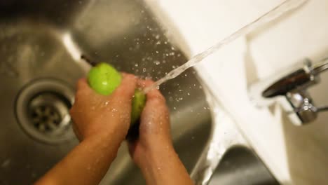 hands washing a pear in a sink