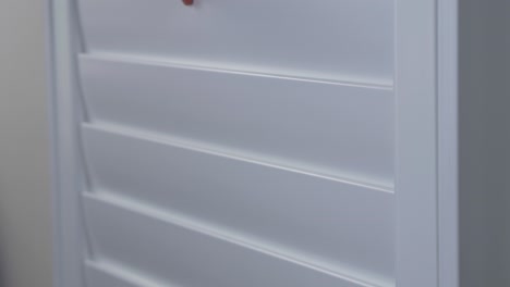 close-up shot of plantation shutters window frame slats being closed with hands in house interior design wall kitchen privacy security protection 4k