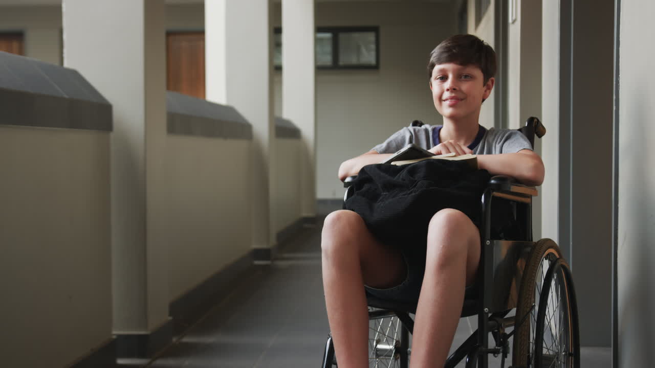 In school, boy in wheelchair holding book, sitting in hallway, looking thoughtful, copy space
