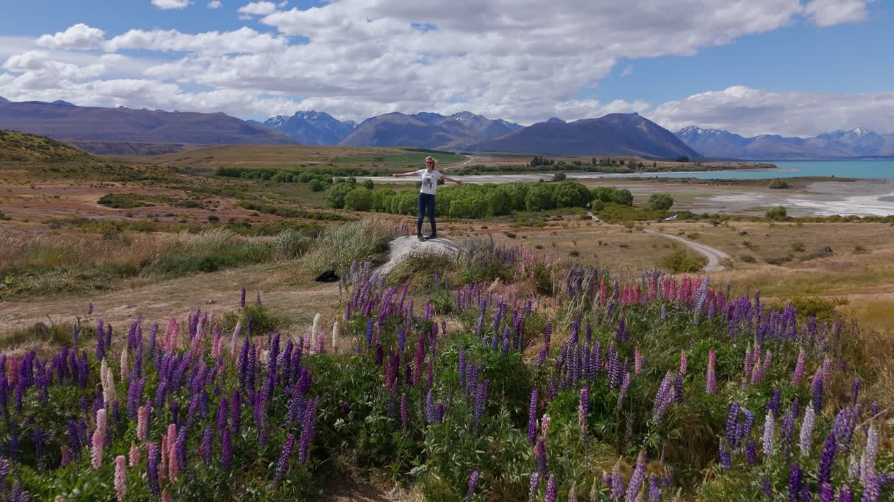 mujer en la roca en el campo de flores de lupino, hermoso paisaje del lago de zelanda