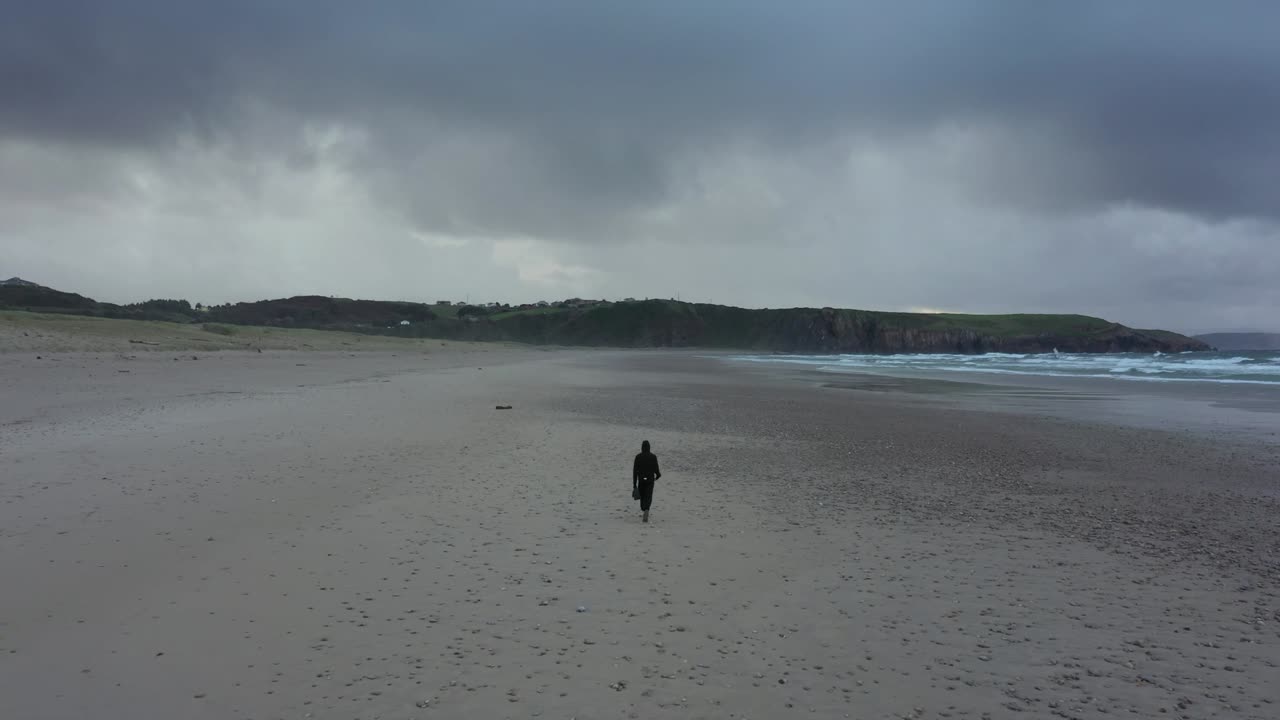 vista trasera del hombre caminando solo en una playa desierta vacía en un día nublado de invierno