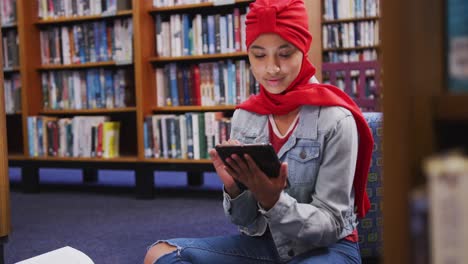 Eine-Asiatische-Studentin,-Die-Einen-Roten-Hijab-Trägt-Und-In-Einer-Bibliothek-Studiert-Und-Ein-Tablet-Benutzt