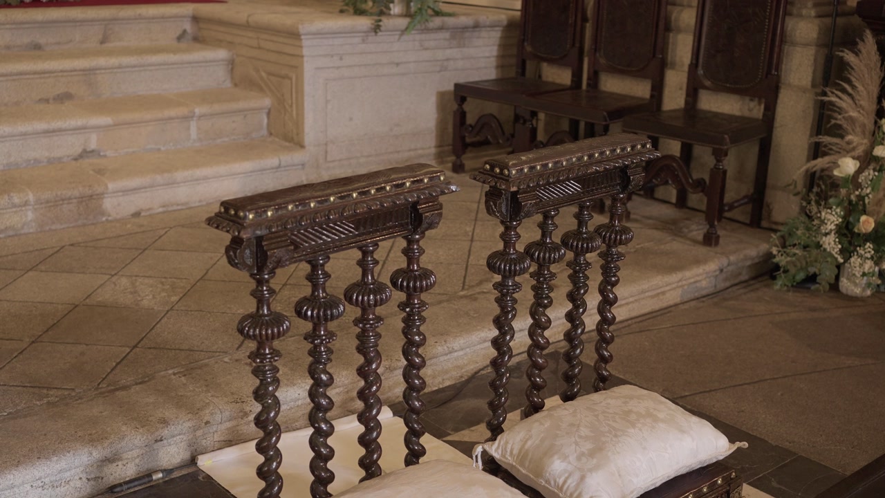 Ornate wooden prayer kneelers with white cushions inside church