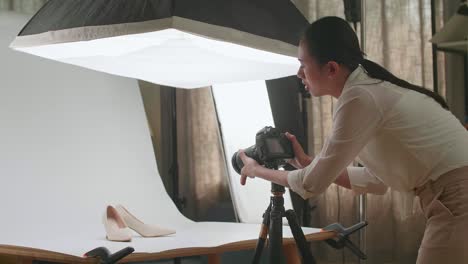 asian female photographer thinking about women's shoes position then raising her index finger while taking photos of them in home studio