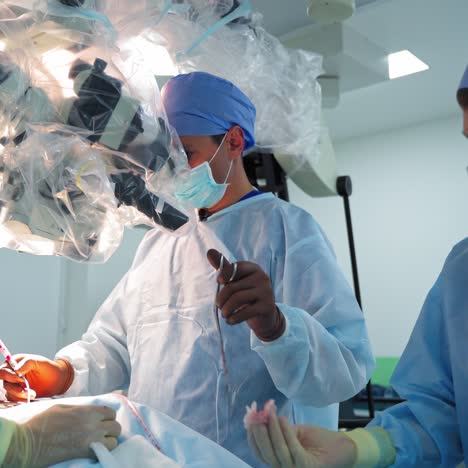 teamwork of surgeons during operation. male specialist looking through the microscope while perform the surgery with medical instruments.