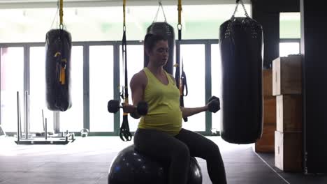 modelo femenino embarazada haciendo ejercicio con pesas en un gimnasio para mantenerse en forma en su cuarto trimestre