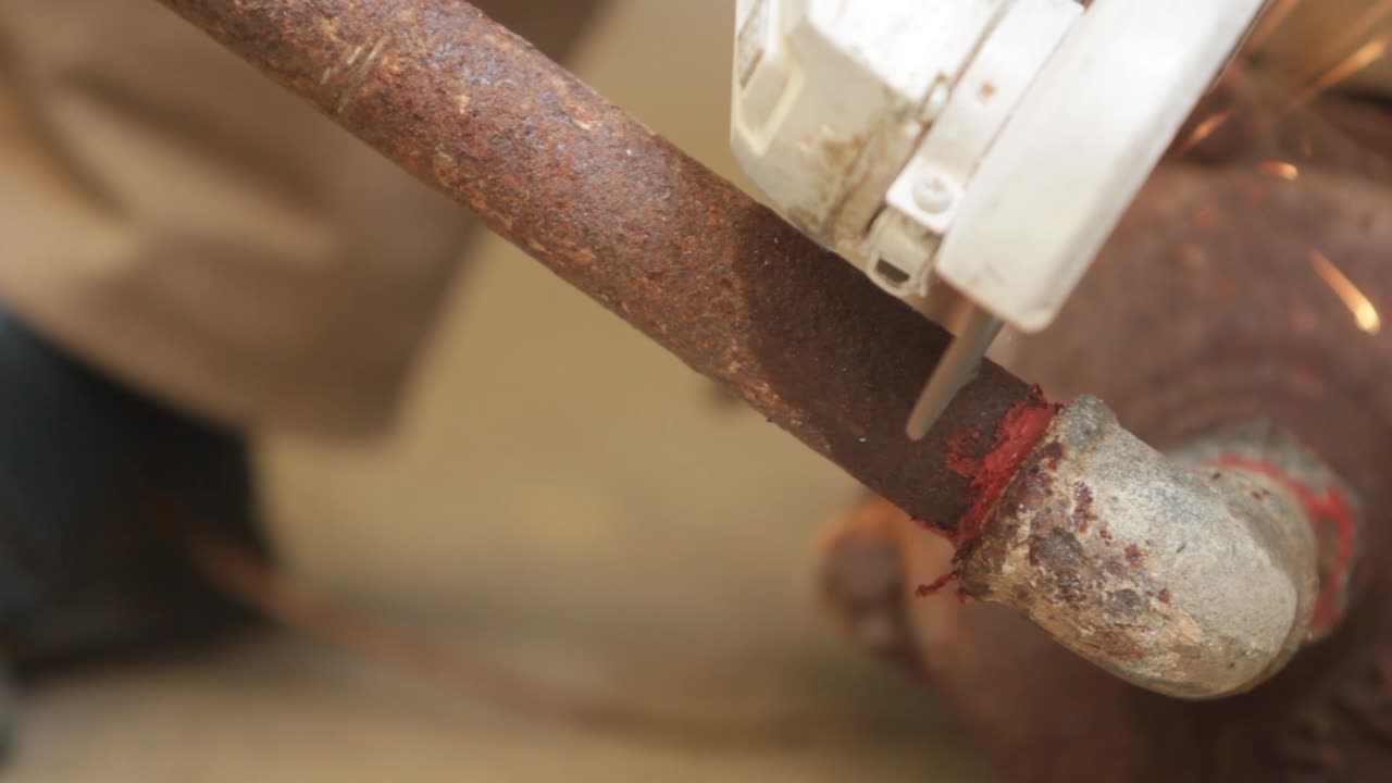 front view of a man picking up a portable grinding machine to cut a rusty metal pipe. Bright sparks