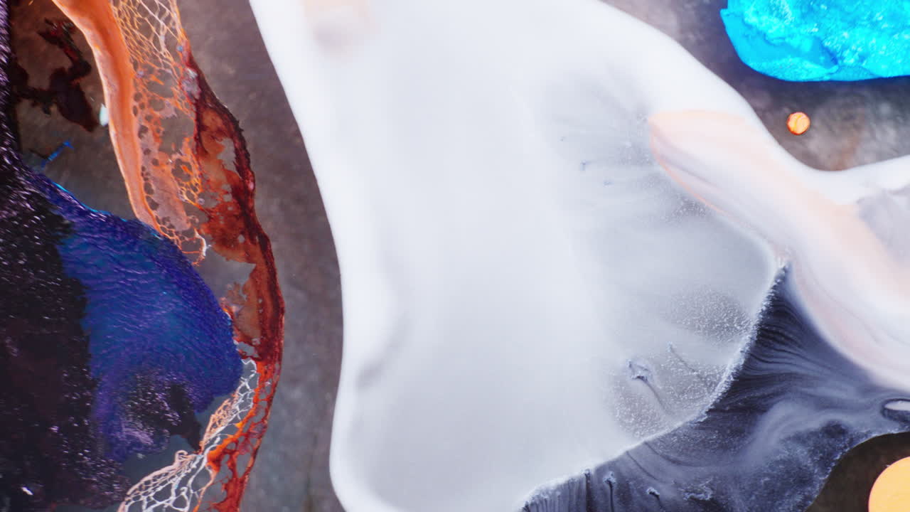 Macro shot of white ink pouring down on liquid medium with other multicolor inks