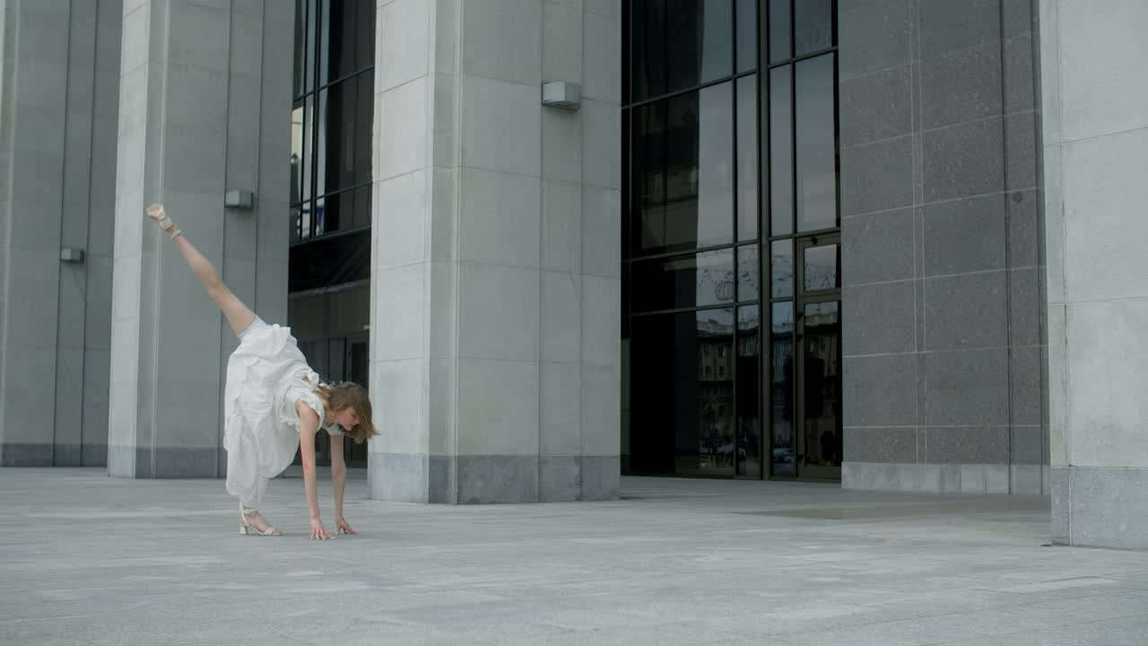 Acrobatic dancer in white dress outside a modern building