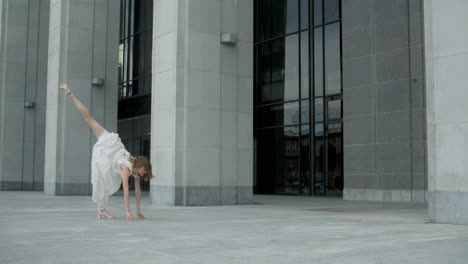 acrobatic dancer in white dress outside a modern building