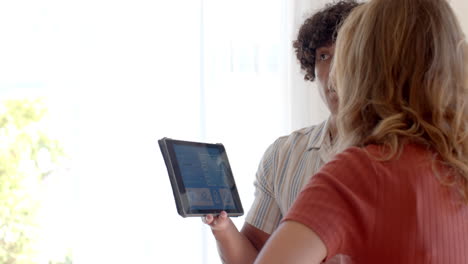 diverse couple discussing vacation plans using tablet at home, enjoying leisure time, copy space