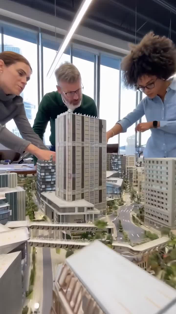 Vídeo em ângulo superior de uma equipe diversificada examinando um modelo urbano em um ambiente de escritório moderno