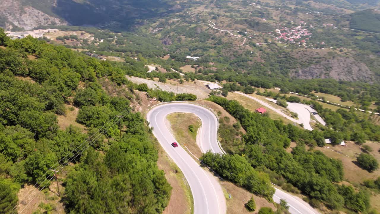 Car driving down a curvy road followed by drone from distance, aerial