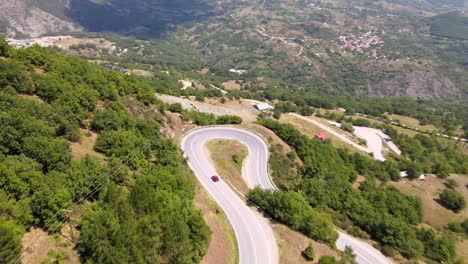 car driving down a curvy road followed by drone from distance, aerial