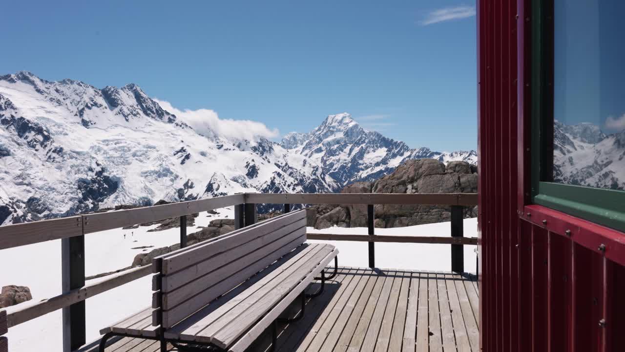 Wooden bench and porch with snowy mountains and Mount Sefton in background on a clear sunny summer day in Mueller Hut, Mount Cook National Park, New Zealand.